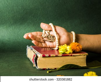 Open Hand Showing Aum Locket With Beads, Rested On A Hindu Scripture Or Book On Green Background, Side Angle