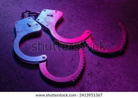 Open handcuffs on a dark background illuminated with a colored mixed light of red and blue