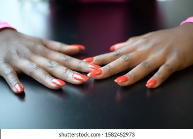 Open hands of a black woman with fingernails painted red on a black table and a pink reflection on the table