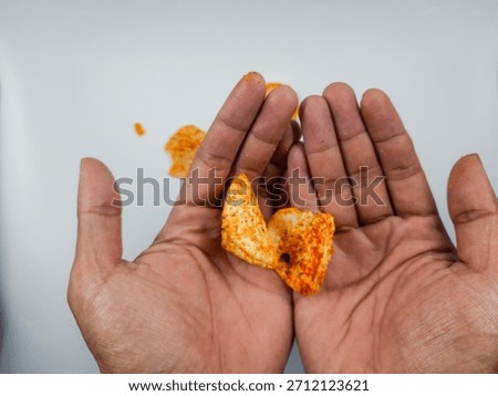Open hands gently cradle two pieces of bright orange seasoned snack chips against a clean white surface suggesting a moment of simple indulgence or a craving for savory flavor.