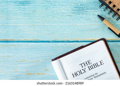 Open Holy Bible Book on a wooden table background with a pen and notebook. Copy space. Top view. Flat lay. Studying old and new testament Scriptures by God Jesus Christ. Christian biblical concept. - Shutterstock ID 2163148989