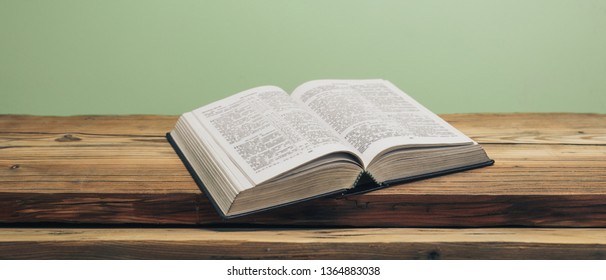 Open Holy Bible On A Old Oak Wooden Table.  Green Wall Background.	