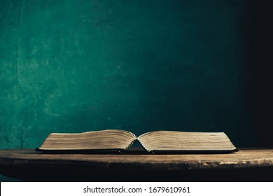 Open Holy Bible On A Old Round Wooden Table. Beautiful Green Wall Background.