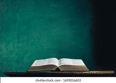 Open Holy Bible On A Old Round Wooden Table. Beautiful Green Wall Background.