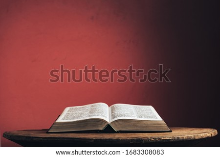 Open Holy Bible on a old brown round wooden table. Beautiful red wall background.