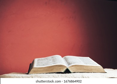 Open Holy Bible on a table. Beautiful red wall background.