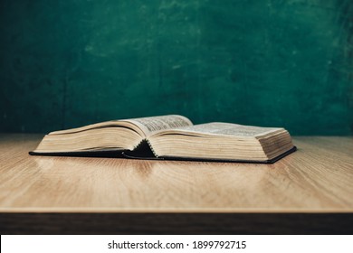 Open Holy Bible On A  Wooden Table. Beautiful Green Wall Background.