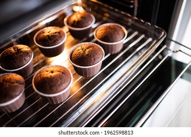 Open Home Oven With Chocolate Tasty Muffins In Baking Forms On Tray At Home. Making Fresh Cupcakes In Stove Close Up. 