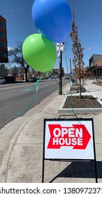 Open House sign with green and blue balloons next to city street