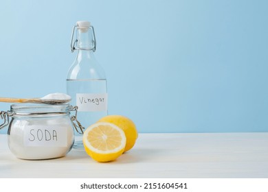 Open Jar Of Baking Soda With A Wooden Spoon On Top, Vinegar, Cut Lemon, On A Blue Background. The Concept Of Organic Removing Stains On Clothes. 