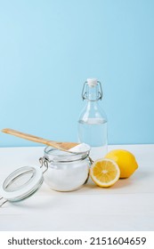 Open Jar Of Baking Soda With A Wooden Spoon On Top, Vinegar, Cut Lemon, On A Blue Background. The Concept Of Organic Removing Stains On Clothes. 