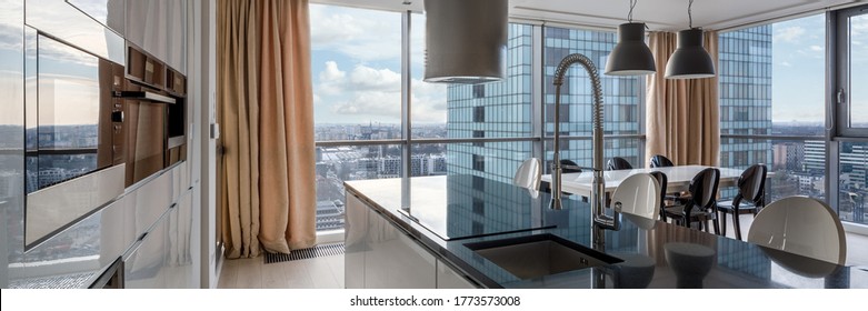 Open kitchen with black countertop, white cupboards and big windows and city view - Shutterstock ID 1773573008