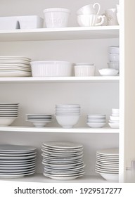 An Open Kitchen Cupboard With Organized White Dishware