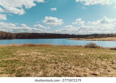 Open Lakeside Meadow Beneath Dramatic Sky Offers Expansive Vista Of Grass And Still Water, Soft Clouds Above Horizon Suggest Fresh Spring Day