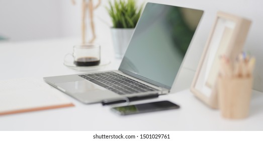 Offener Laptop-Computer mit Bürobedarf und Bürodekorationen auf weißem Schreibtisch am minimalsten Arbeitsplatz
