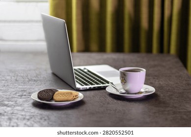 Open laptop computer on a table with a cup of hot chocolate and a plate of cookies