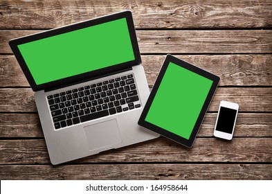 Open laptop with digital tablet and white smartphone. All with isolated screen on old wooden desk.