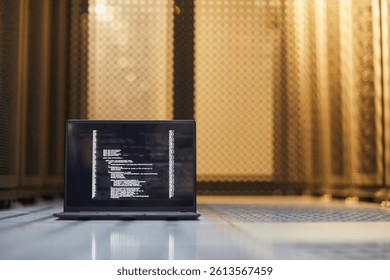 Open laptop displaying lines of code against backdrop of server racks in dim lighting. Scene represents data processing, programming, and technology infrastructure maintenance