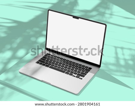 Open laptop with empty white display on a pastel mint surface, palm leaf shadows softening the minimalist composition for a clean product mockup.