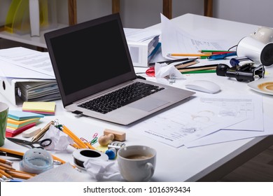 An Open Laptop On The Messy Desk With Coffee Cup And Documents At Workplace