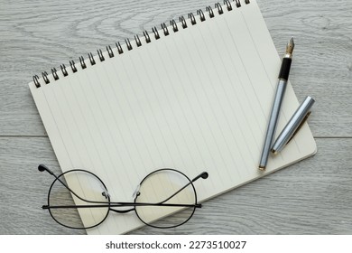 An open laptop and other office equipment such as a pen and glasses. on a wooden office table. - Shutterstock ID 2273510027