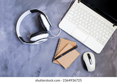 An open laptop stands on a table on a gray background, next to it lies a notepad, a pen, white headphones and a computer mouse.  Concept of office work, online training, webinars.  Flat laying. - Shutterstock ID 2364936725