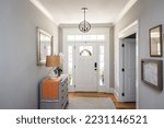 An open large and wide interior front door hallway foyer with transom, hanging light fixture, coastal colors and entry way table and wood floors.
