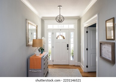 An open large and wide interior front door hallway foyer with transom, hanging light fixture, coastal colors and entry way table and wood floors. - Shutterstock ID 2231146521