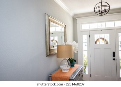 An open large and wide interior front door hallway foyer with transom, hanging light fixture, coastal colors and entry way table and wood floors.