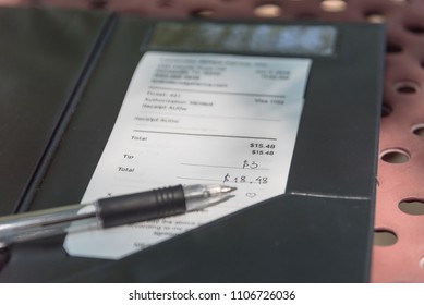 Open leather bill holder with restaurant check and pen. Soft focus receipt with hand written total amount and tipping on outdoor picnic table, natural light. Paper invoice with suggested gratuities - Powered by Shutterstock