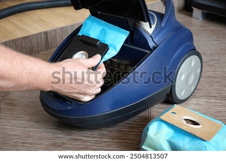 Open the lid of the vacuum cleaner to replace the dust container. Against the background of the apartment interior. Installing a dust bag into a vacuum cleaner.