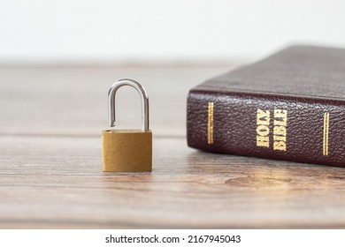 Open lock (padlock) and closed Holy Bible Book on a wooden table with white background. Security, protection, safety in God Jesus Christ, Christian biblical concept. A close-up.