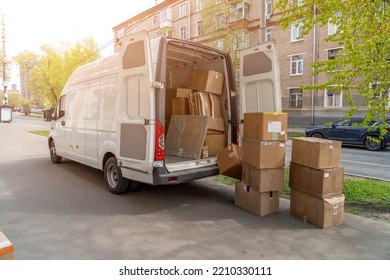 Open Lorry Car Trunk With Moving Cardboard Packages Outdoors. White Delivery Van And Many Different Cardboard Boxes At City Street.