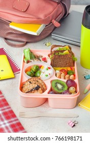 Open Lunch Box With Healthy Lunch With Sandwiches, Vegetable Salad, Fresh Grape And Kiwi, Rice With Grilled Brussels Sprouts And Nuts On The Table Near School Backpack; Selective Focus