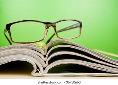 Open magazines and glasses in composition lying on table on green background - Powered by Shutterstock