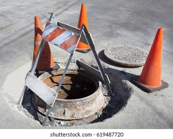 Open Manhole Sewer Pipe With Orange Safety Cones And Wooden Barricade.