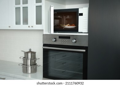 Open microwave oven with food on white shelf in kitchen - Shutterstock ID 2111760932