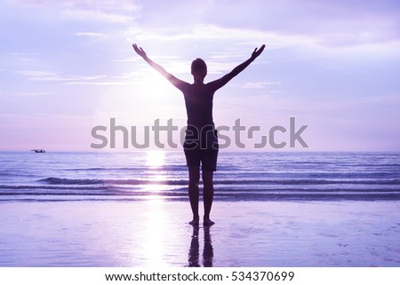 Open mindedness and happiness concept. Woman's silhouette on sunset beach. Stretched out hands to the sky. 