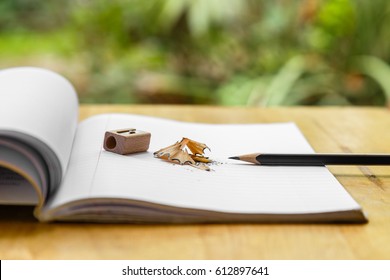 Open note book with pencil, sharpener and shavings on wooden and green background.