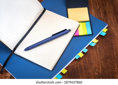 Open Notebook With Blank Lined Pages And Blue Ballpoint Pen Lying On Top Of Blue Covered Textbook Marked With Lots Of Post It Notes