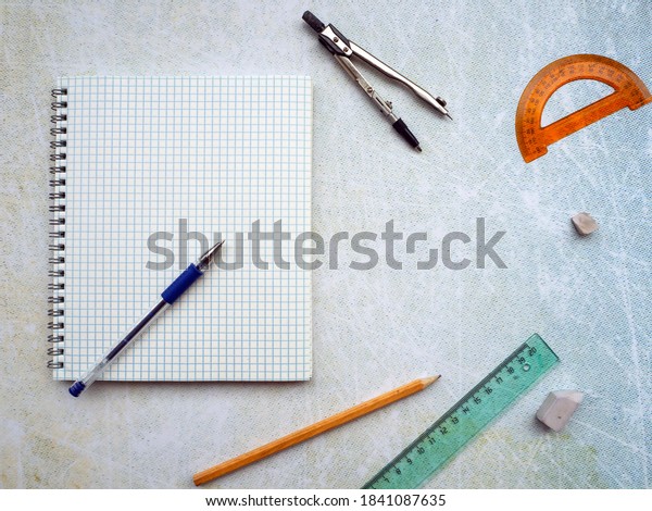 Open notebook with blank page. There is a\
blue pen on the notebook. The compass, ruler, pencil and protractor\
are next to the notebook. Empty\
space.