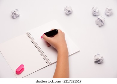 an open notebook and blank pages  human hand holds pink marker   some crumpled pieces paper the white background