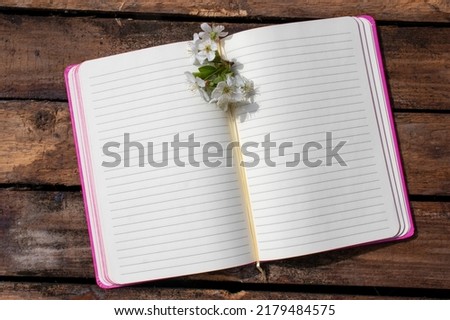 Open notebook with blank paper lined pages and cherry blossom flowers on wooden table background. Spring, summer memories, girl's diary. Top view, flat lay, copy space 