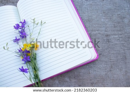 Open notebook with blank paper lined pages and wild flowers on wooden table background. Spring, summer memories, girl's diary. Top view, flat lay, copy space, close up 