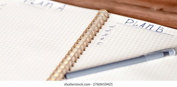 Open notebook displaying handwritten notes for plans A and B, with a gray pen placed on a wooden table surface