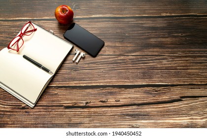 Open notebook with empty pages and other office supplies, glasses a smartphone and a red apple on a wooden desk table. Top view, plan and copy space
 - Powered by Shutterstock