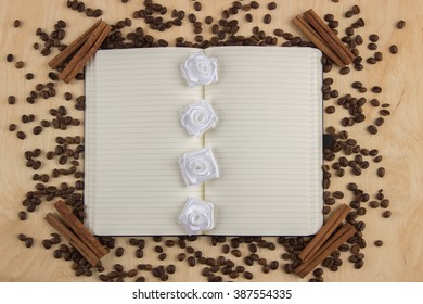 Open notebook with lined pages on a wooden table on which are scattered coffee beans and flowers lie and cinnamon