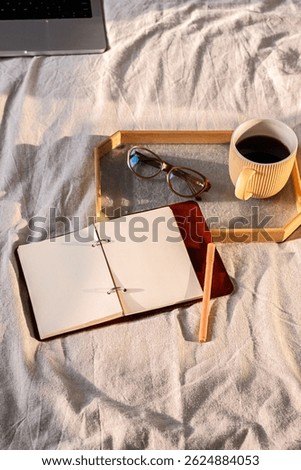 Open Notebook on Bed with Coffee Cup, Glasses and Laptop. Cozy Morning Scene for Writing and Planning.