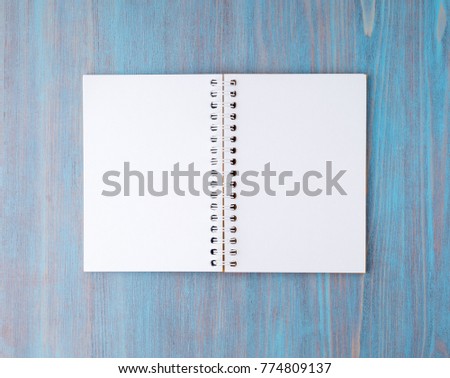 Open notebook on spring with white paper for notes and drawing. Light background, blue wood, top view.