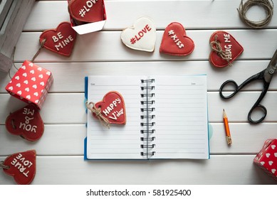 Open notebook on white wooden table with cookies in form of heart. St. Valentines Day concept. Eye bird view